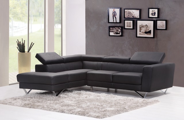 modern black leather couch in a living room with a large window and dark grey wall